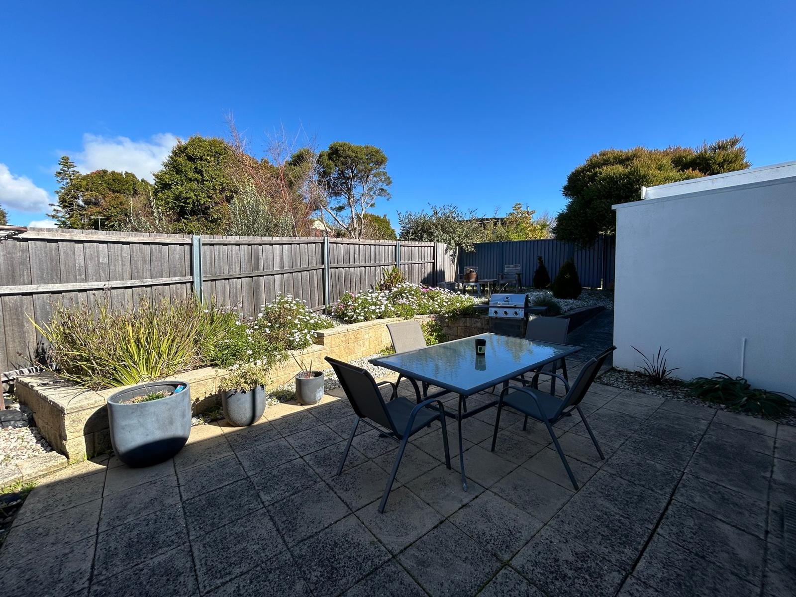 Private paved courtyard with outdoor dining setting, garden beds and barbeque